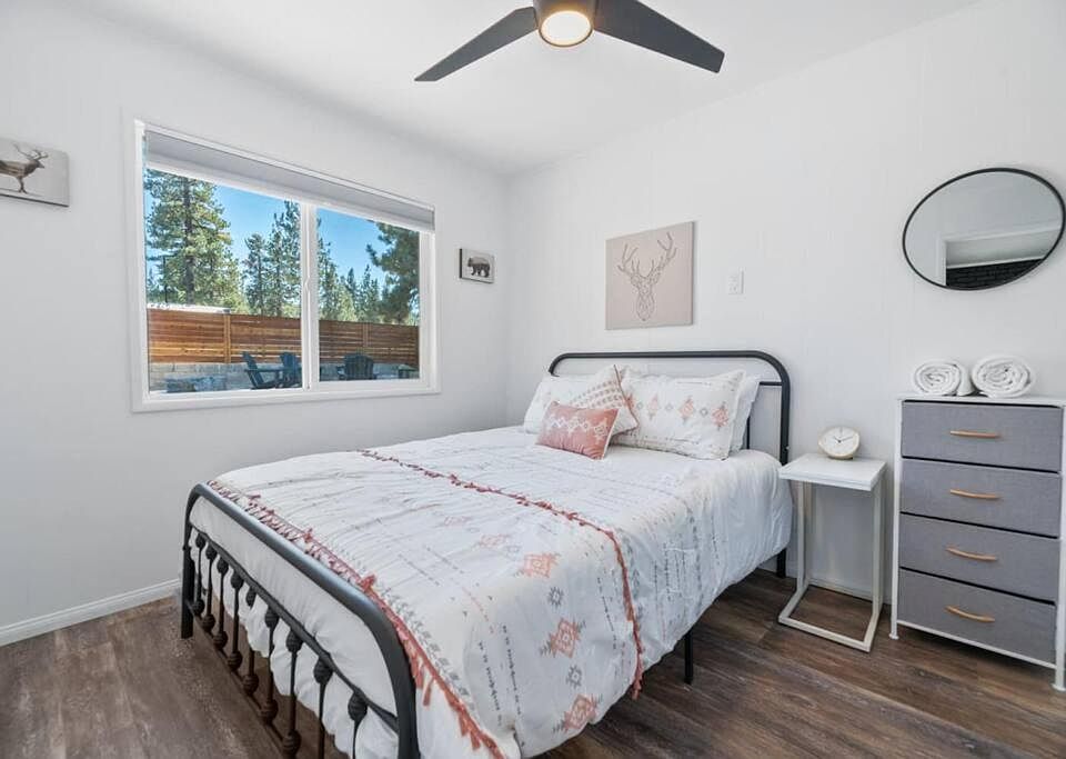 Furnished bedroom with a full bed, ceiling fan, and dresser, plus a large window with outdoor views for added light.