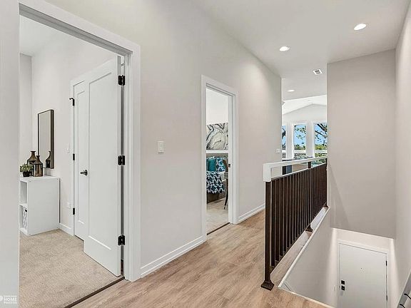 Hallway: Bright open hallway with engineered hardwood floors, clean white doors, and modern stair railing