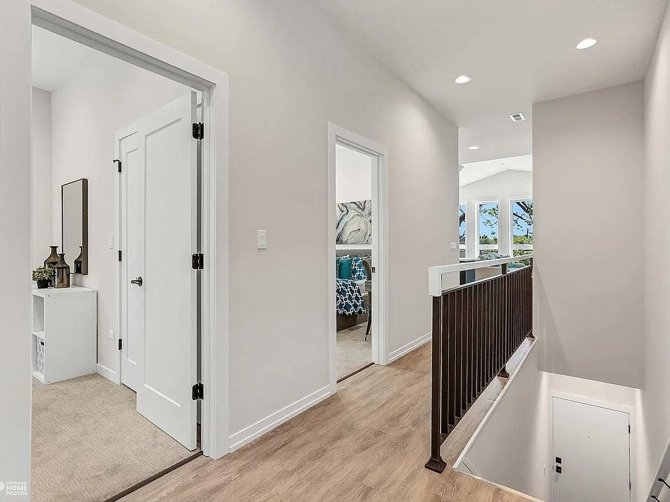 Hallway: Bright open hallway with engineered hardwood floors, clean white doors, and modern stair railing