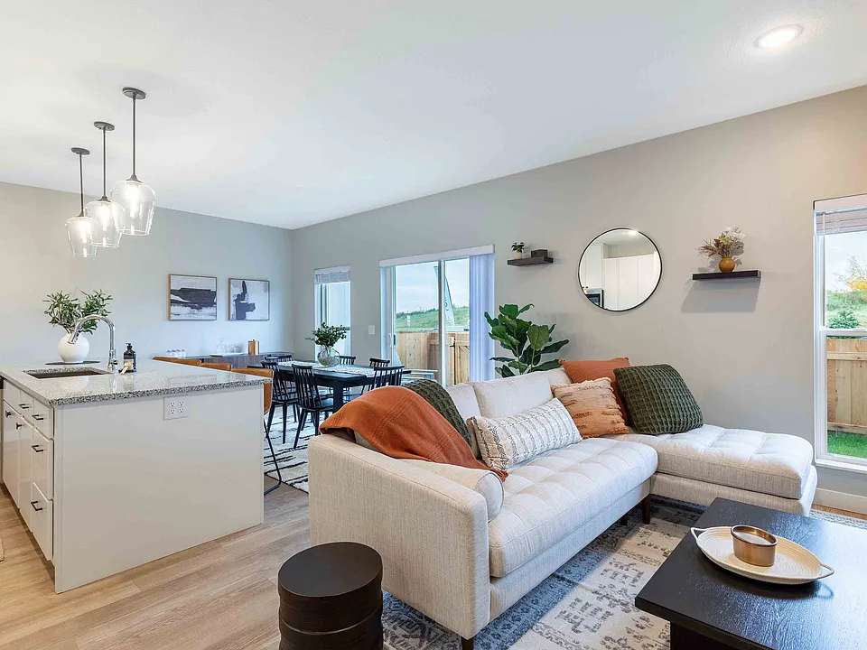 Modern living space featuring a cozy sectional sofa with elegant cushions, a sleek kitchen island with pendant lighting, and a spacious dining area opening to a scenic view.