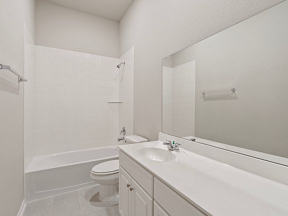 The secondary bath features tile flooring, white cabinetry and light countertops and a shower tub co