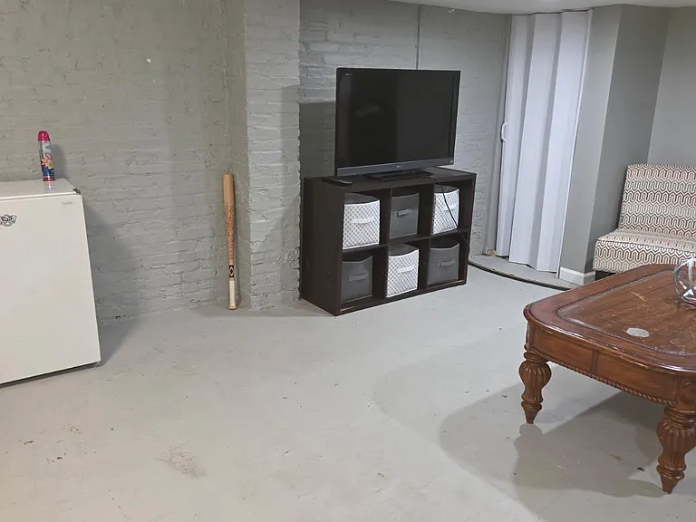 Finished lower-level flex space with concrete floors, storage cubbies, and a seating/TV area for relaxing or hobbies.