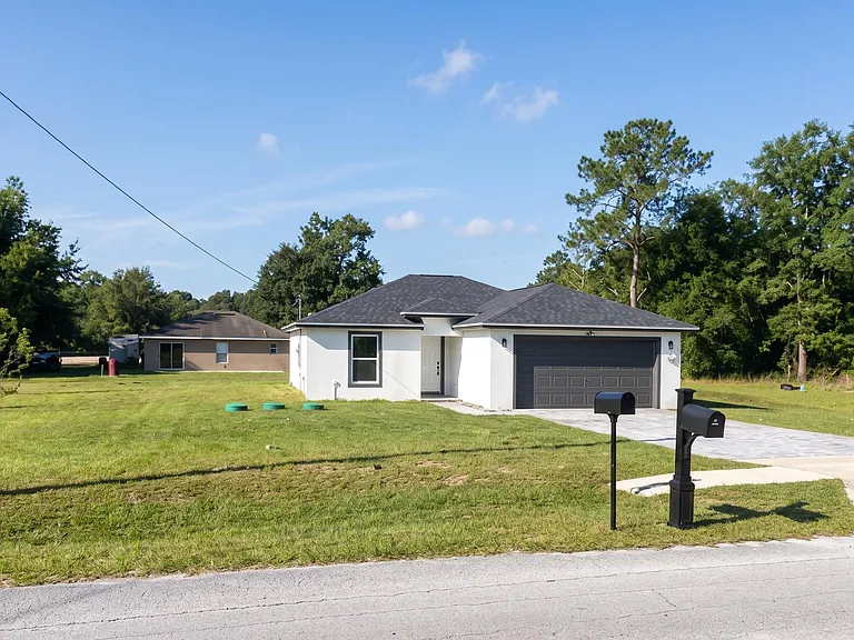 Single-story home with a wide driveway, two-car garage, and a large open front yard framed by mature trees.