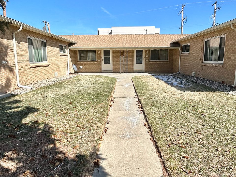 Charming brick apartment complex with a sunny courtyard and inviting walkway, offering warmth and community living.