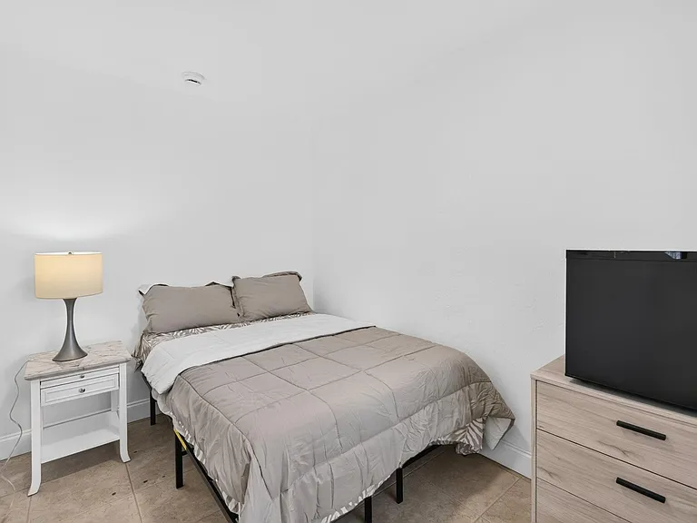 Furnished bedroom with a full-size bed, nightstand with lamp, and dresser topped with a mini fridge for added convenience.