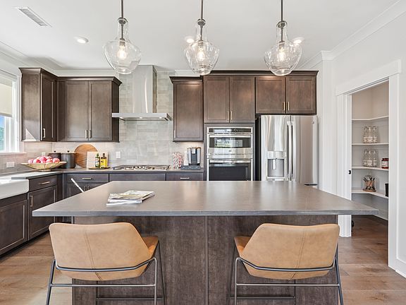 A modern and spacious kitchen with dark wood cabinets, a large island with seating, and pendant ligh