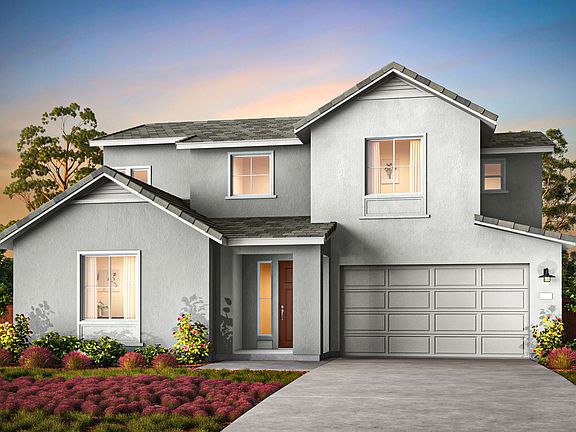 A two-story gray house with a garage door, surrounded by a lush garden and a colorful floral display