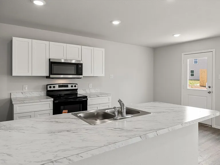 Kitchen featuring white shaker cabinetry, stainless steel microwave, black electric range, and stone-finish countertops with an integrated double basin sink