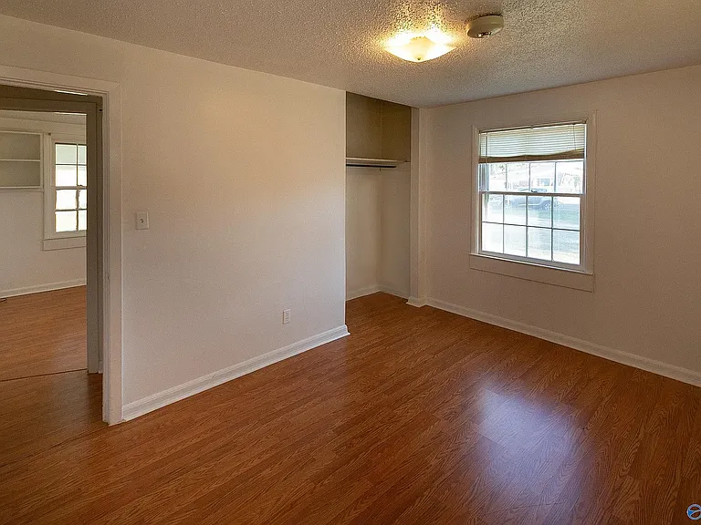 View of the master bedroom showing, from left to right, the door into the room (with the 2nd bedroom across the hall), the closet in the back corner (no closet door), and the side window. There is another window to the right, shown in the next photo.