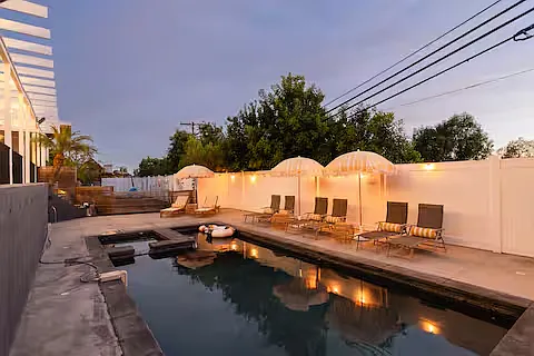 Resort-style outdoor space with a heated pool, hot tub, sun loungers with umbrellas, and cozy seating. Perfect for relaxing, sunbathing, or enjoying poolside drinks, this stylish area offers a luxurious retreat for ultimate leisure.