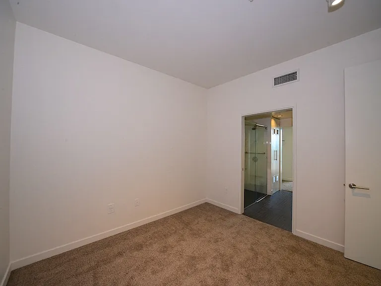 Carpeted bedroom with access to bathroom at 12th Street Lofts in National City, California.