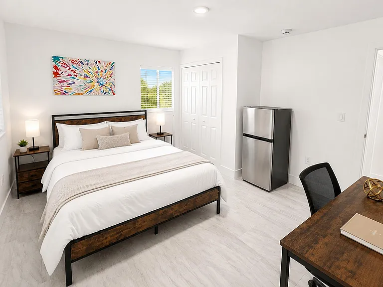Spacious furnished bedroom with private bath, large windows, a work desk, ample closet storage, and an in-room mini fridge.