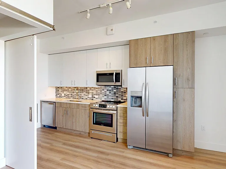 Apartment Kitchen with Stainless Steel Appliances, Quartz Countertops and Wood-Style Flooring.