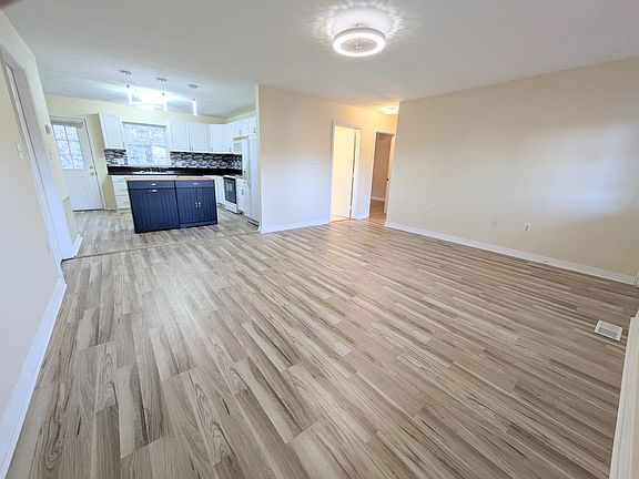 Open-Concept Entry: Step through the front door into a bright, open living space featuring brand-new laminate flooring and a direct view of the spacious kitchen