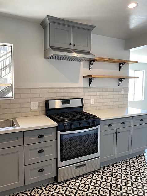 Stainless steel range with cast iron grates; quartz countertops, designer tile work, and open/floating shelves