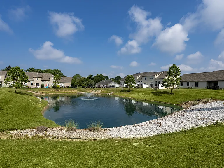 Relax by a peaceful pond surrounded by lush greenery and charming homes, offering a tranquil setting within the community.