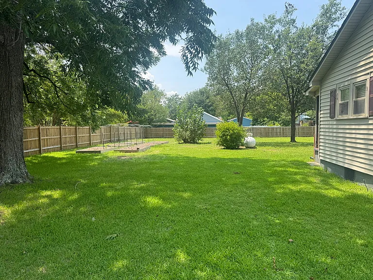 Left Side Yard: Fenced and gated side yard featuring a mature pecan tree and raised garden beds.
