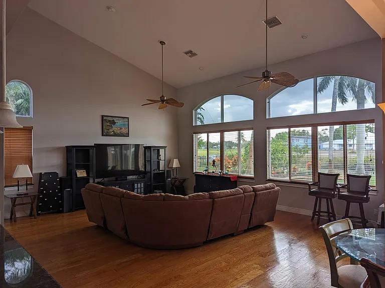 Living room, view from grand entry. The living room has 22-foot ceilings, fans, recessed lighting, water-view, sunrise/sunset view, wood blinds, an 85-inch TV, a BOSE surround sound system and a comfortable sectional that includes 3 built-in recliners