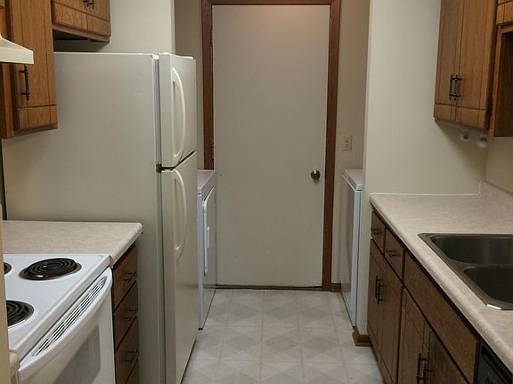 View of the kitchen from the living room - note electric range with vent hood, dishwasher, full-sized fridge, washer, dryer, and tons of cabinet space. Door out to the attached, single car garage.