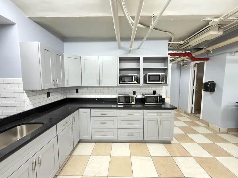 Updated communal kitchenette with ample cabinetry, subway-tile backsplash, generous counters, and multiple microwaves.