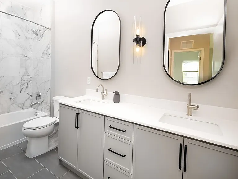 Signature Collection Townhome bath with white quartz countertop, grey cabinetry, vanity mirrors, porcelain shower surround, and hard surface flooring