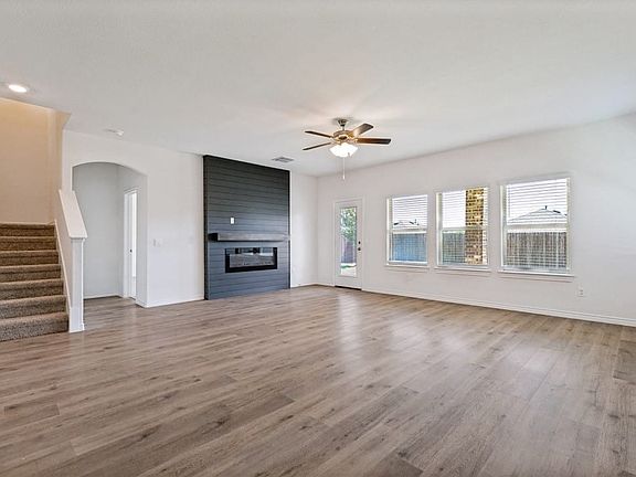 Spacious living area featuring wood-finish flooring, a modern black shiplap fireplace with mantel, and a ceiling fan