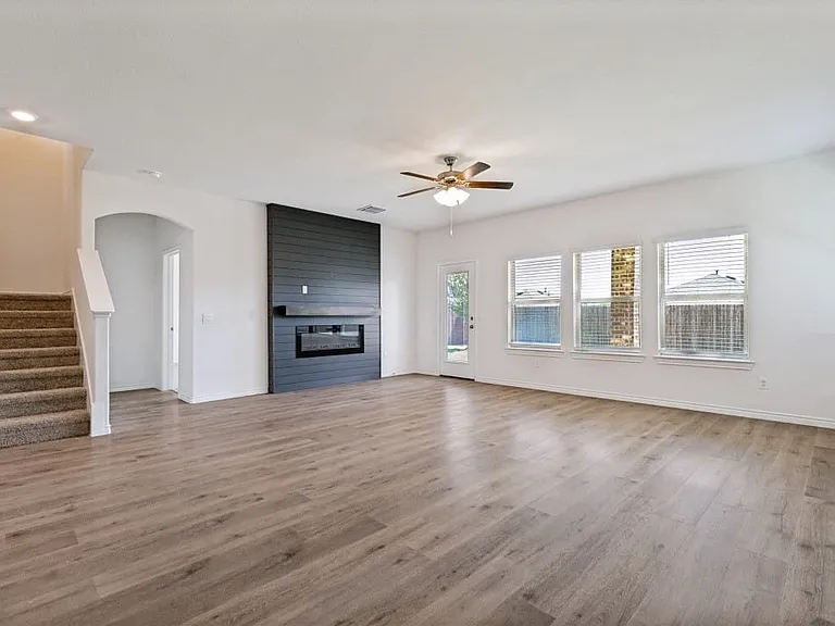 Spacious living area featuring wood-finish flooring, a modern black shiplap fireplace with mantel, and a ceiling fan