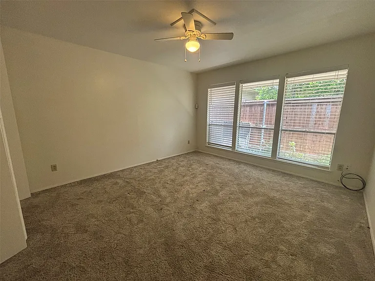 Carpeted room featuring a ceiling fan with light fixture and a wall of three windows with blinds