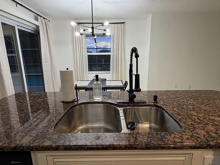 Kitchen features a deep double-basin sink, expansive granite-look counters, and an adjacent dining nook with large windows.
