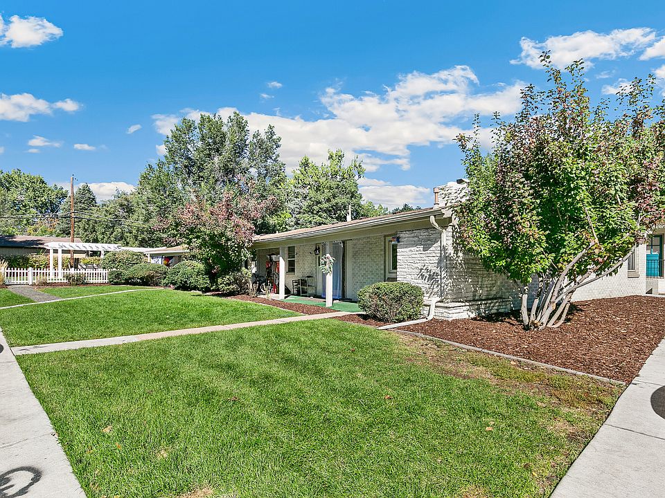 Charming single-story home with lush green lawn, mature trees, and inviting front porch, under a bright blue sky.