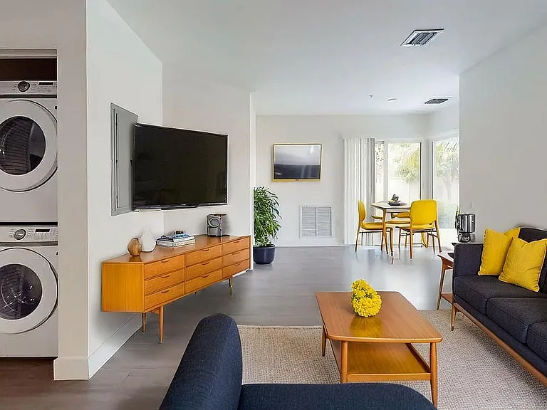 Modern living room with stylish mid-century furniture, bright yellow accents, and a convenient in-unit washer dryer. Open dining area with natural light.