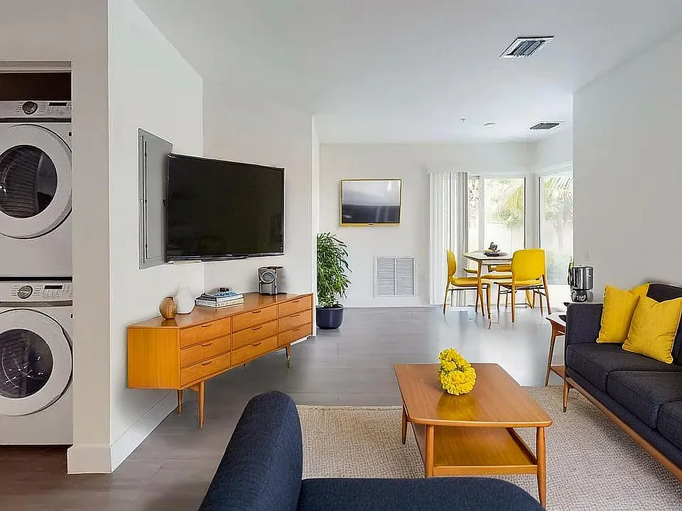Modern living room with stylish mid-century furniture, bright yellow accents, and a convenient in-unit washer dryer. Open dining area with natural light.