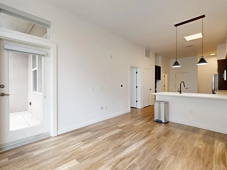 Apartment kitchen with stainless steel appliances, dining and living room with wood-style flooring.