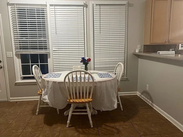 Eat-in dining area with a round table setup, large windows with blinds, and convenient pass-through to the kitchen.