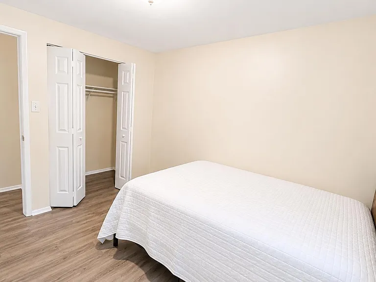 Bedroom with wood-look flooring, a closet with shelving, and space for a full/queen bed plus additional furniture.