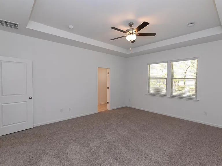 Another view of the bedroom showcasing plush carpet and bright natural light from the windows.