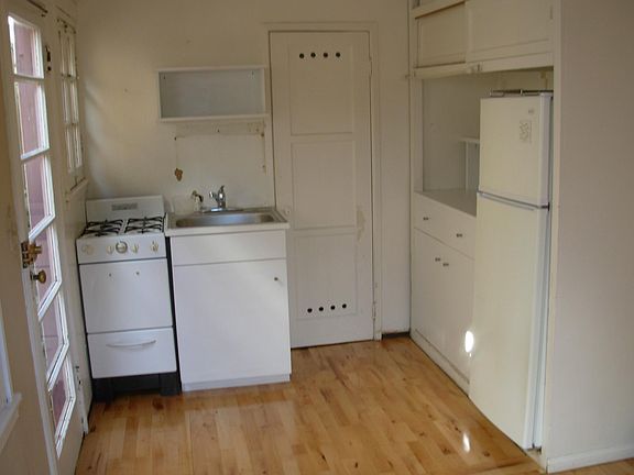 Kitchen area with small range, refrigerator, and cupboard space.