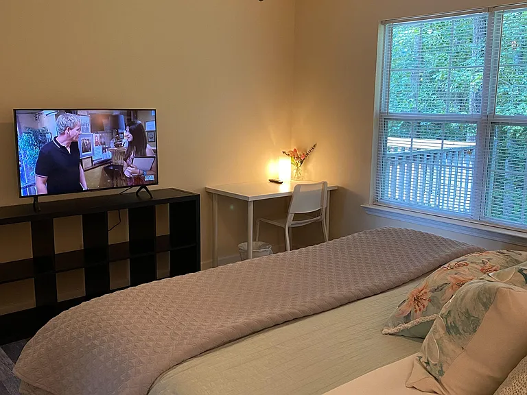 Comfortable bedroom with a full bed, ceiling fan, and a dedicated desk workspace beside a large window.