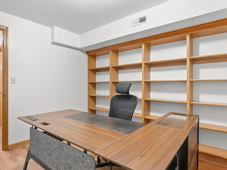 Dedicated basement office with a spacious desk, ergonomic chair, and extensive built-in shelving for a comfortable and organized workspace.