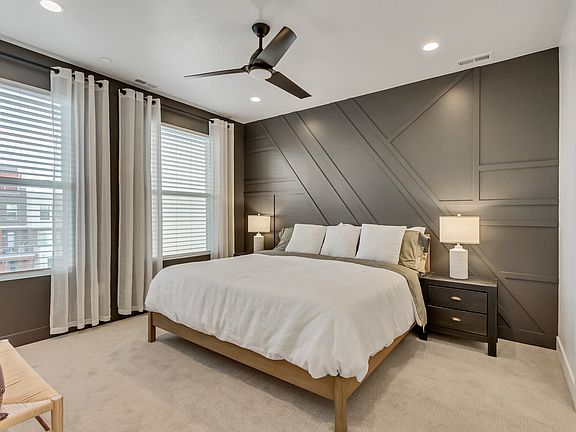 Modern bedroom with a white bed, gray accent wall, two bedside tables with lamps, and large windows