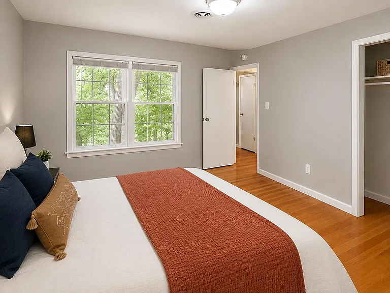 Spacious bedroom with hardwood floors, large window for natural light, and an open closet with shelving for storage.