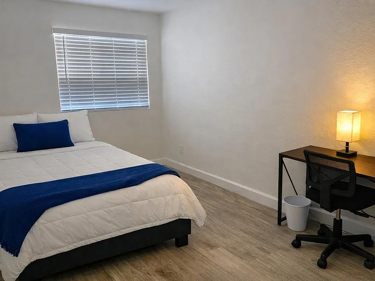 Private bedroom with a full bed, window blinds, and a dedicated desk setupideal for sleeping and working at home.