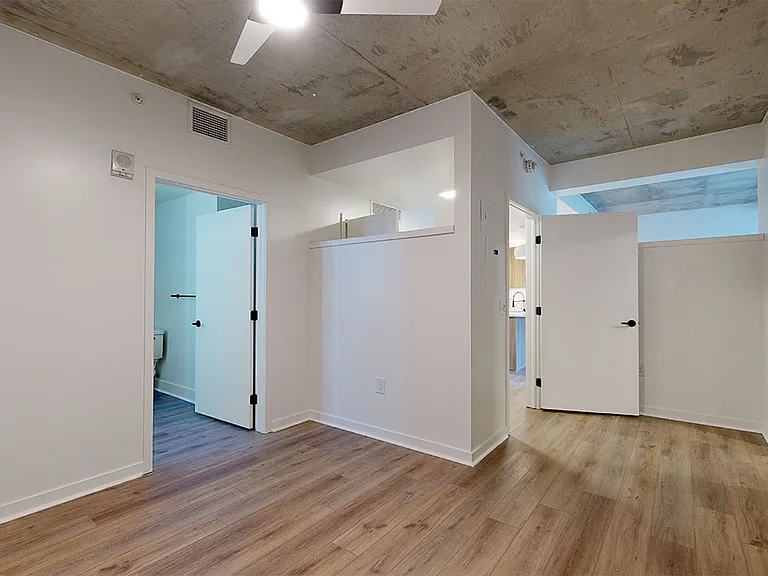 Spacious apartment bedroom with large closet, attached bathroom and wood-style flooring.