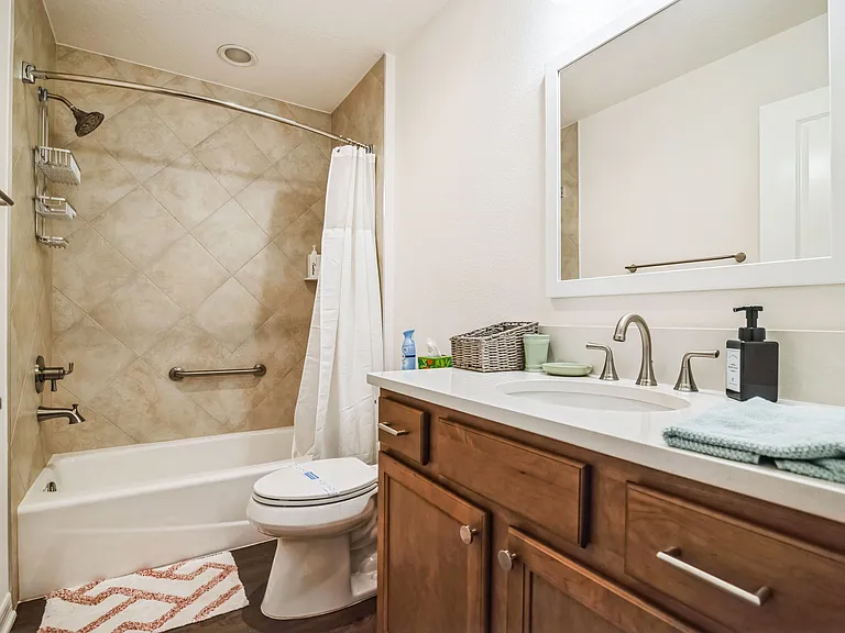 Primary and Secondary Bedroom Shared Bathroom with an Oversized Countertop with Sink and Mirror, Tiled Shower, and Bathtub Handle Bar.
