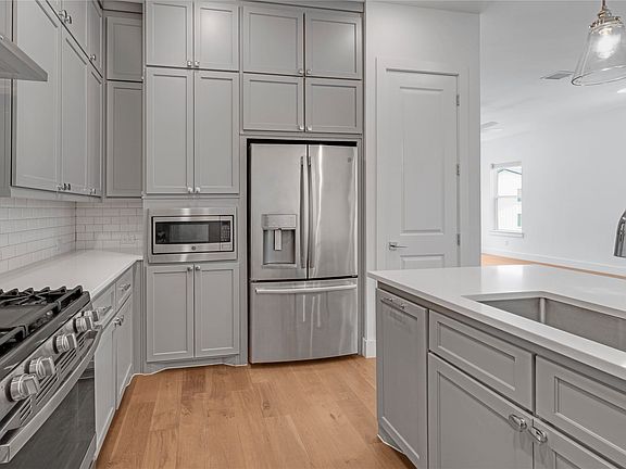 Kitchen featuring light gray cabinetry, stainless steel appliances, a subway tile backsplash, and light wood-finish flooring