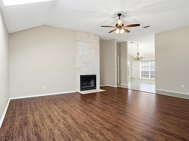 Spacious room featuring wood-finish flooring, a vaulted ceiling, and a fireplace with a stone surround