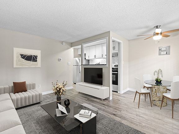A modern living room with a white sofa, a glass coffee table, and a dining area