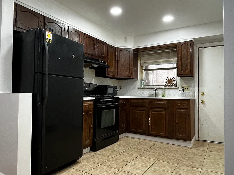 Spacious kitchen featuring brand-new granite countertops, durable tile flooring, plenty of wood cabinetry, full-size black appliances, and direct access to the back patio