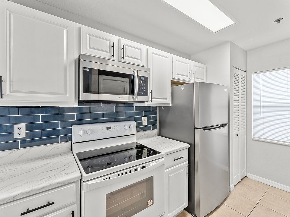 Modern kitchen with sleek stainless steel appliances, glossy white cabinetry, and elegant blue tiled backsplash.
