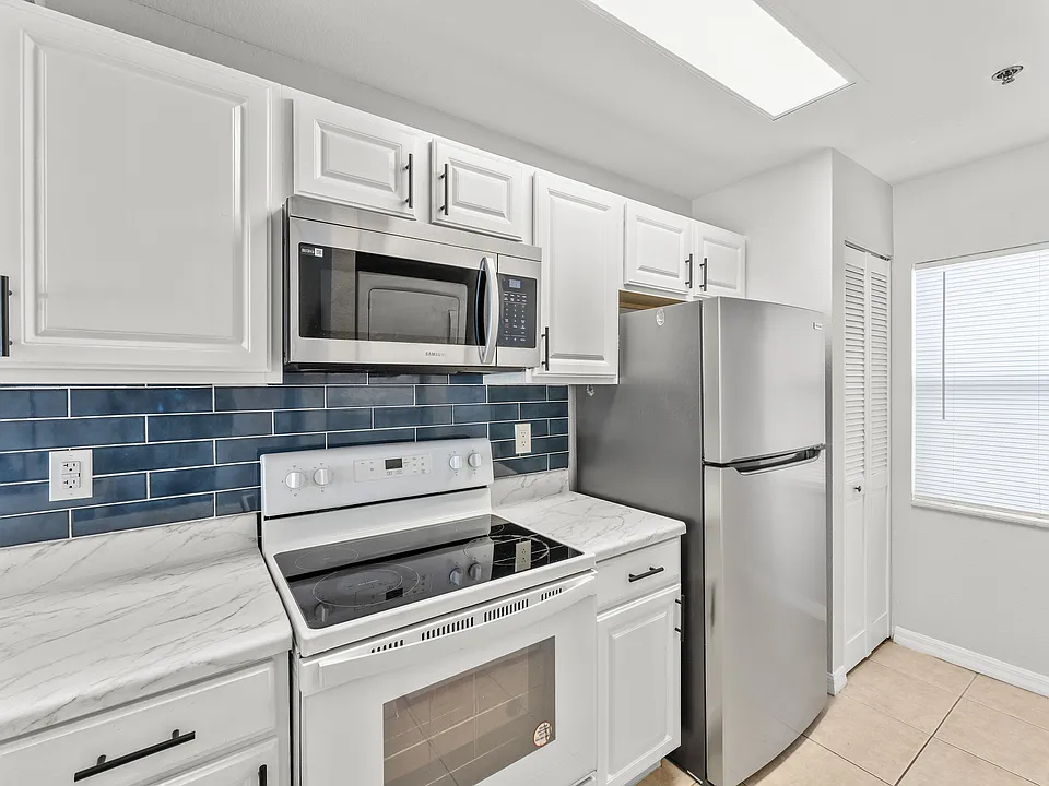 Modern kitchen with sleek stainless steel appliances, glossy white cabinetry, and elegant blue tiled backsplash.